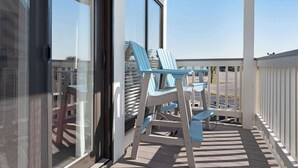 En balkon med et bord og stole, udsigt til himlen og en bygning i baggrunden.