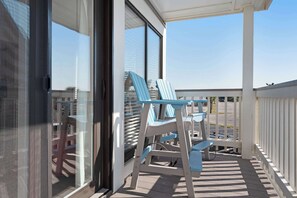 A balcony with a table and chairs, a view of the sky, and a building in the background. - Waterfront condo with pool & hot tub (Fort Morgan)