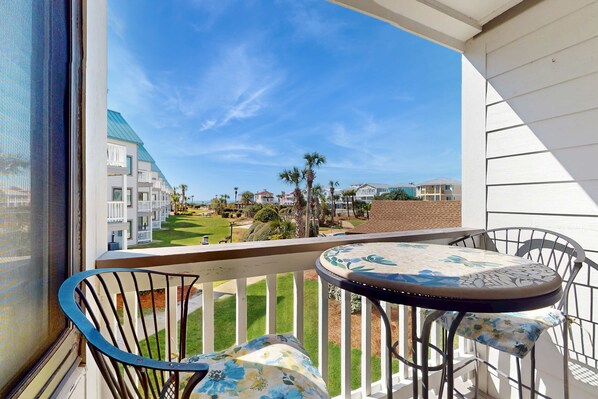 A balcony with a table and chairs, overlooking a well-maintained lawn and buildings. - Lovely condo with balcony & gym - great for couples retreat (Fort Morgan)