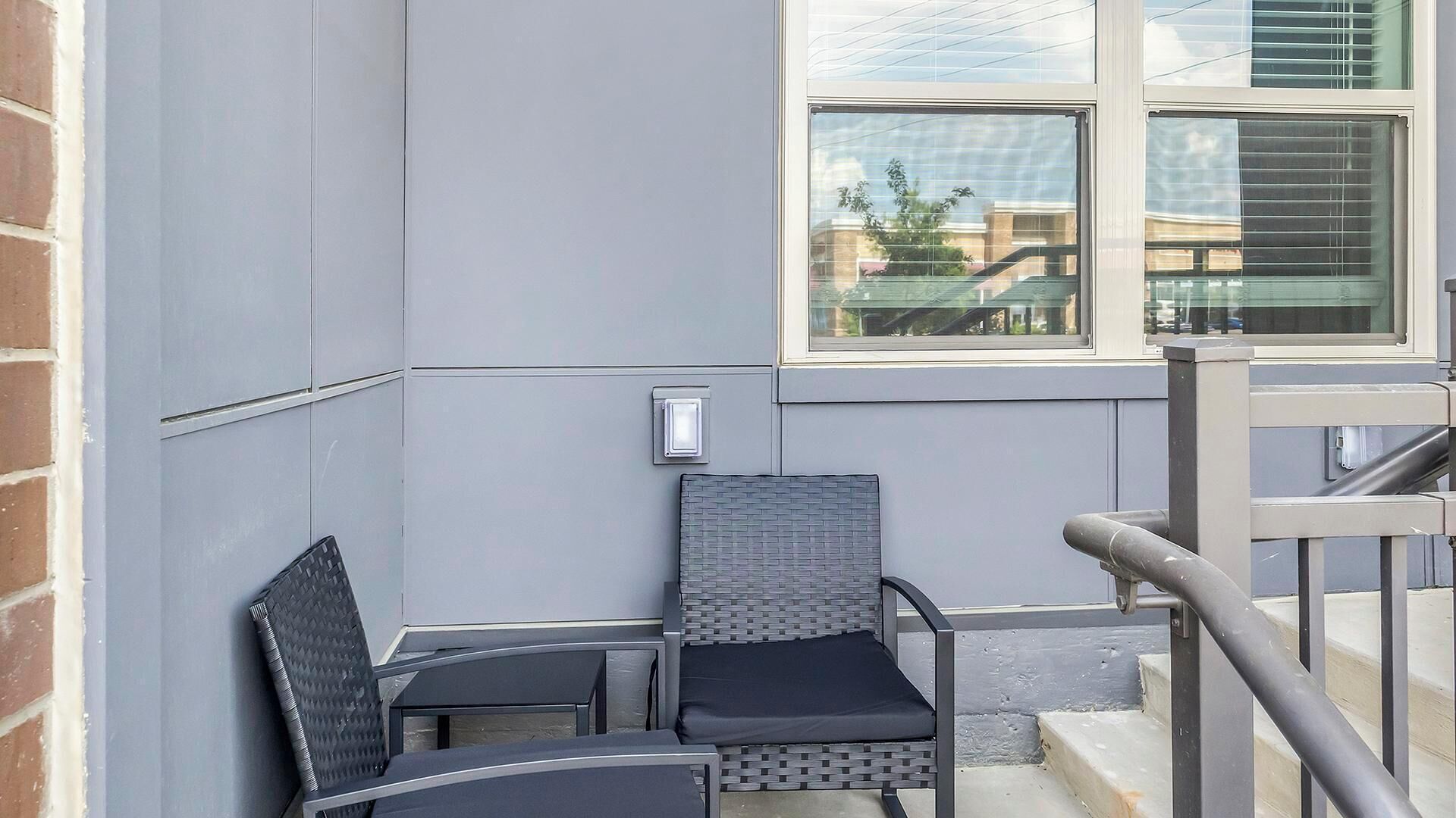Una esquina de un edificio con un muro gris, una ventana y una barandilla metálica.