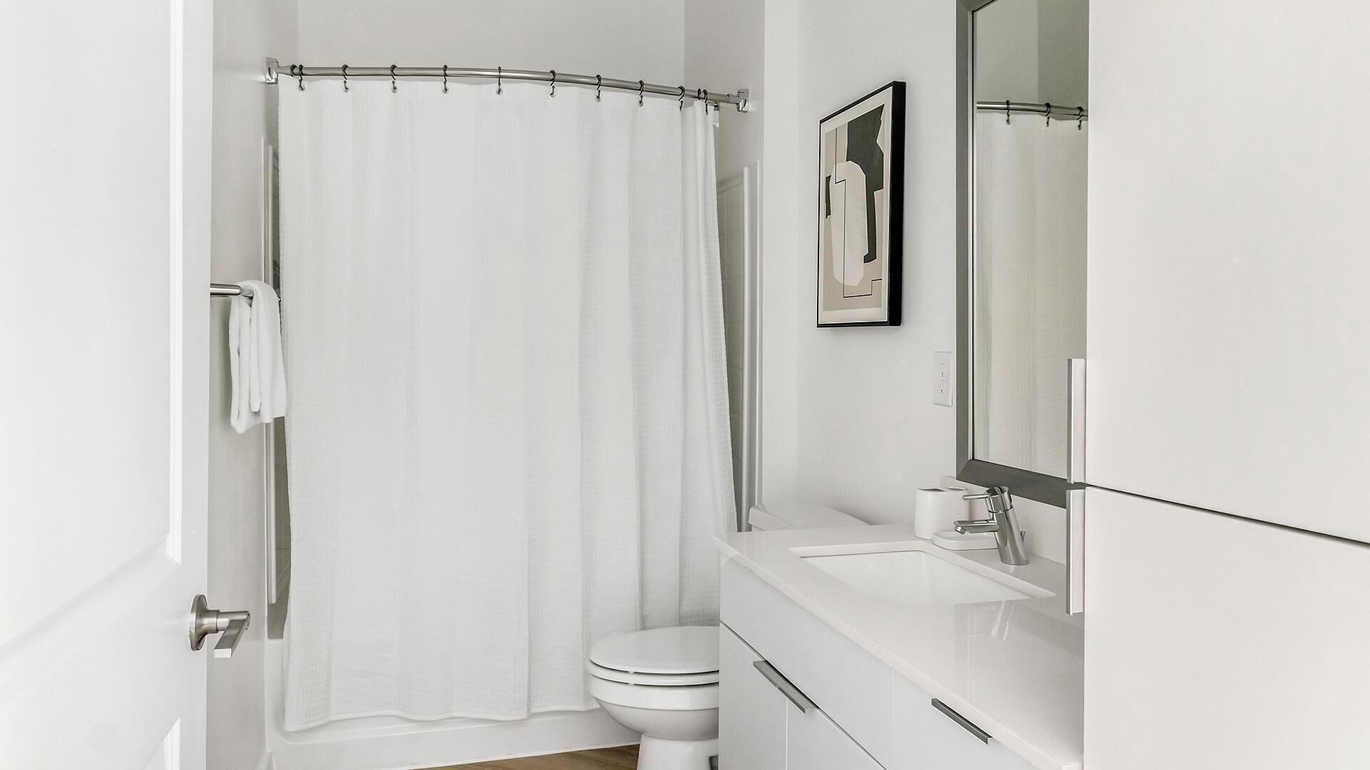 Ein modernes Badezimmer mit Duschvorhang, Toilette, Waschbecken und Spiegel.