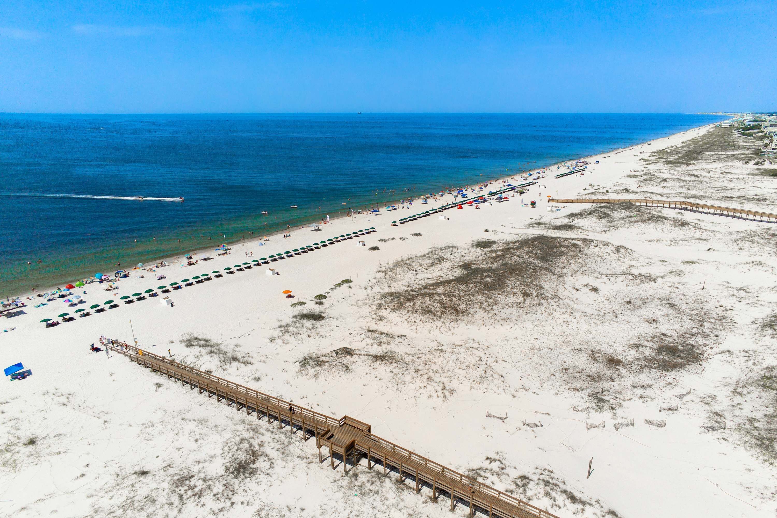 Une plage avec une jetée en bois, des zones de sable et un ciel bleu dégagé.