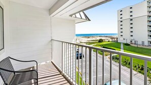 A balcony with a view of the beach and a parking area.