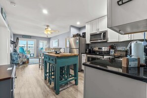 A modern kitchen with a central island, stainless steel appliances, and a ceiling fan. - Hotel condo features beach access, shared pool - near town (Fort Morgan)