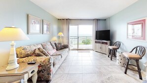 Ein Wohnzimmer mit Sofa, zwei Sesseln, Fernseher, Lampe und Balkon.