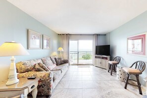 Ein Wohnzimmer mit Sofa, zwei Sesseln, Fernseher, Lampe und Balkon.