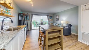 A modern kitchen with granite countertops, a wooden dining table, and a view to the outdoors. - Waterfront condo with shared pool & hot tub - near dining & the beach (Fort Morgan)