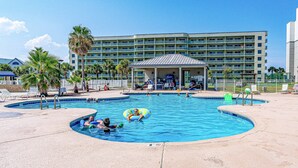 A hotel with a swimming pool, lounge chairs, and palm trees. - Waterfront condo with shared pool & hot tub - near dining & the beach (Fort Morgan)