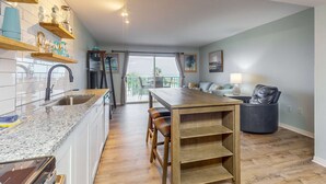 A modern kitchen with granite countertops, wooden shelves, and a dining area with a wooden table and chairs. - Waterfront condo with shared pool & hot tub - near dining & the beach (Fort Morgan)