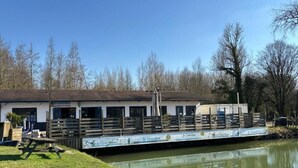A riverside building with a dock, a picnic table, and a signboard.