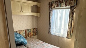 A compact RV interior with two beds, a small table, and a window with curtains.