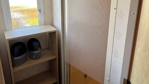 A bathroom with a shower, a shelf with two buckets, and a window with blinds.