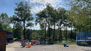 A gravel area with outdoor seating, a small building, and a lake surrounded by trees.