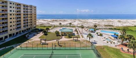 Un hotel de varios pisos con cancha de tenis, zona de piscina y vista al mar.