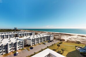 A beachfront hotel with multiple balconies, a parking area, and a view of the beach and ocean. - Plantation Dunes condo with Gulf views, pool, hot tubs & gym - walk to beach (Fort Morgan)
