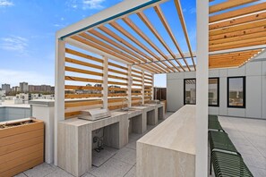 Un bar en la azotea al aire libre con vigas de madera, una barra larga y vistas a la ciudad.