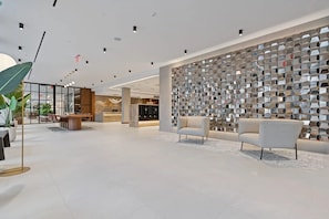 Een moderne lobby met een receptiebalie, zithoek en decoratieve wand.