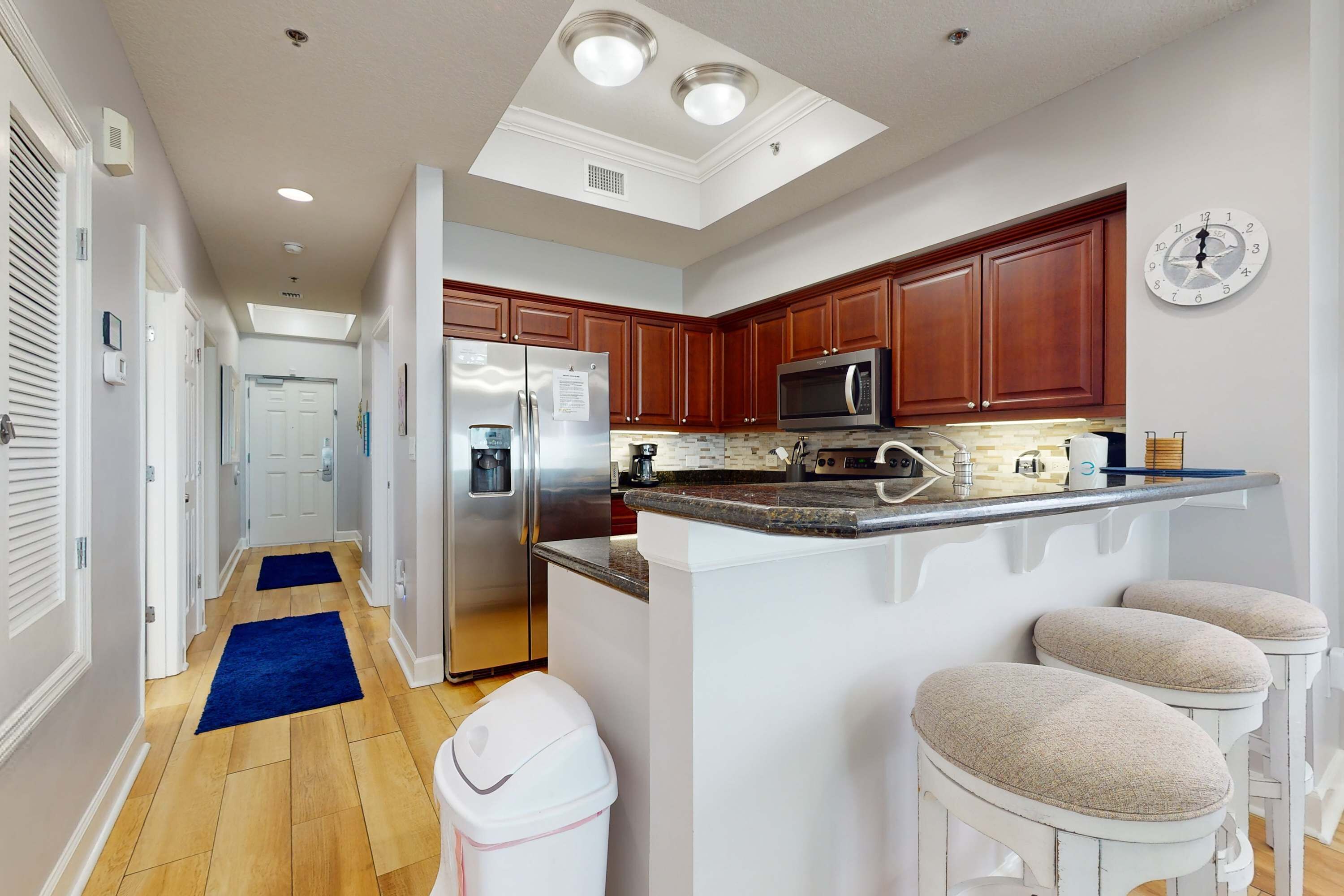 A modern kitchen with wooden cabinets, a stainless steel refrigerator, a microwave, and a bar area with stools.