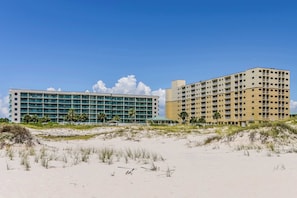 A beachfront hotel with multiple floors, a flat roof, and a sandy beach in the foreground. - Contemporary beachside escape with gym, & pools (Fort Morgan)