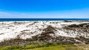 A beach with a wooden fence, sandy dunes, and a clear blue sky. - Third-floor condo with balcony, close beach access, pools, hot tubs & tennis (Fort Morgan)