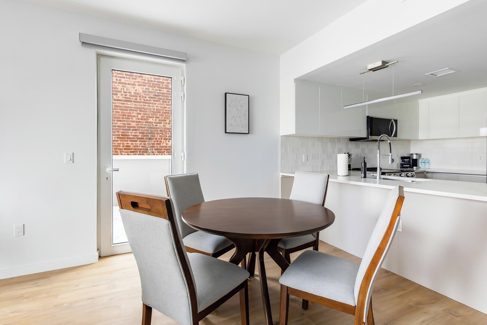 A modern kitchen with white cabinets, a round dining table with four chairs, and a visible brick wall.