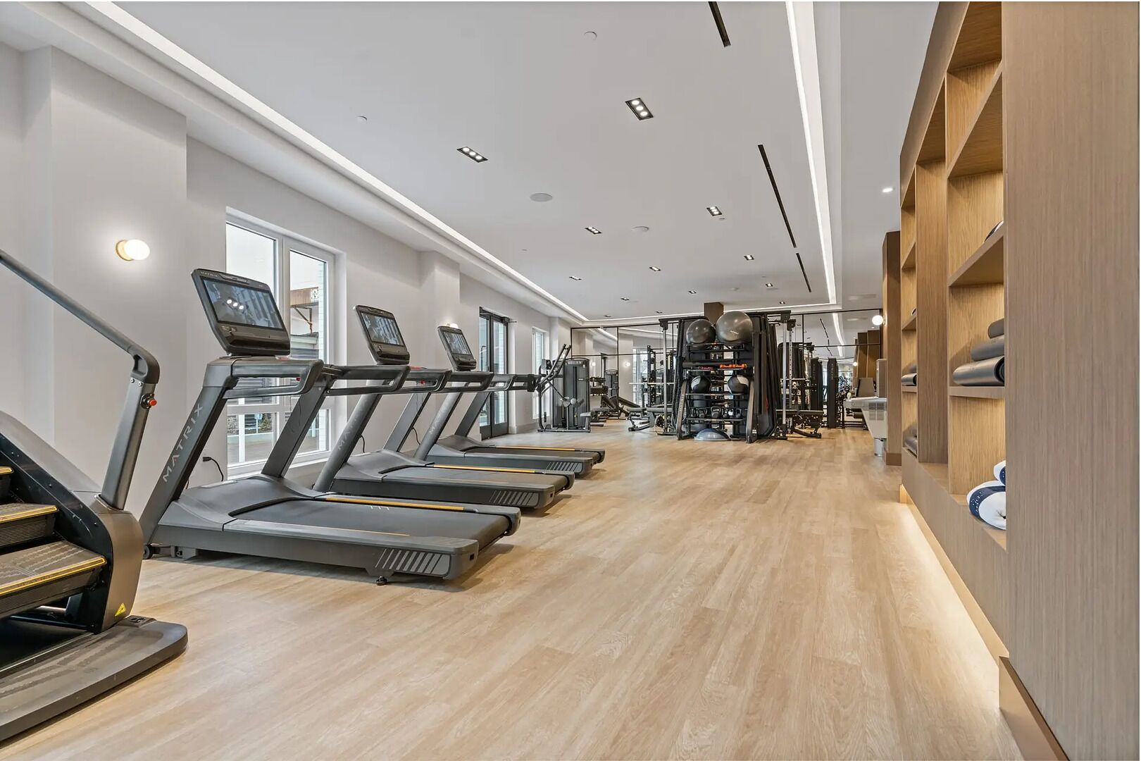 Ett modernt gym med löpband, styrketräningsmaskiner och en väggpanel i trä med förvaringsutrymme.