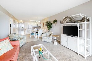 A living room with a sofa, a coffee table, a TV stand, and a dining area with chairs and a table. - Gulf-Facing Condo w Balcony, WiFi, Central AC & Resort Pools Hot Tubs Tennis (Fort Morgan)