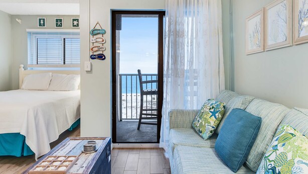 A room with a bed, a sofa, a small table, and a door leading to a balcony with a chair. - Fifth floor oceanfront studio with central AC, WiFi, pools and gym (Fort Morgan)