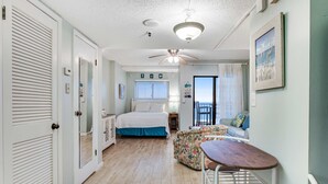 A room with a bed, a sofa, a small table, a ceiling fan, and a window. - Fifth floor oceanfront studio with central AC, WiFi, pools and gym (Fort Morgan)