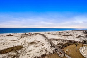Ein Strand mit einer Holzpromenade, die zu einem Sandbereich führt, einem klaren Himmel und dem Meer im Hintergrund.