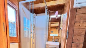 Une petite salle de bain comprenant des toilettes, une douche et un lavabo, avec des murs en bois et une petite fenêtre.