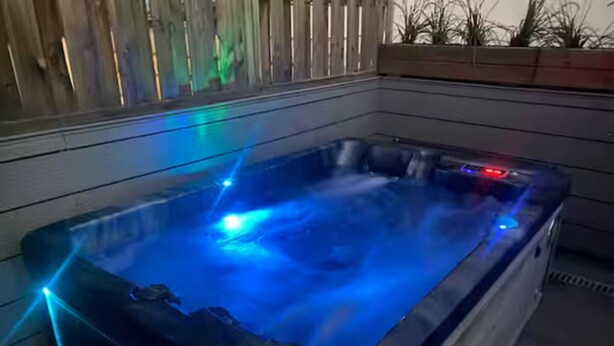 Un bain à remous doté d’un éclairage LED bleu, entouré d’une terrasse en bois et agrémenté d’un jardinière avec des plantes.