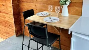 Une pièce aux murs lambrissés, avec une table à manger dressée pour deux personnes, agrémentée d’un vase blanc contenant des fleurs, de deux verres à vin et d’une chaise noire.