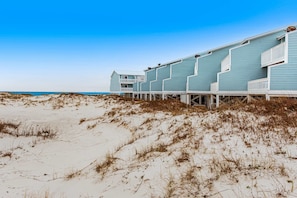 A beachfront hotel with multiple levels, wooden walkways, and a clear view of the ocean. - Gulf-Front: Dolphins, Starlight & Steps to Beach (Fort Morgan)