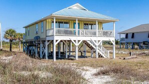 Una casa sulla spiaggia con un balcone, un portico coperto e una scala che conduce al piano superiore.