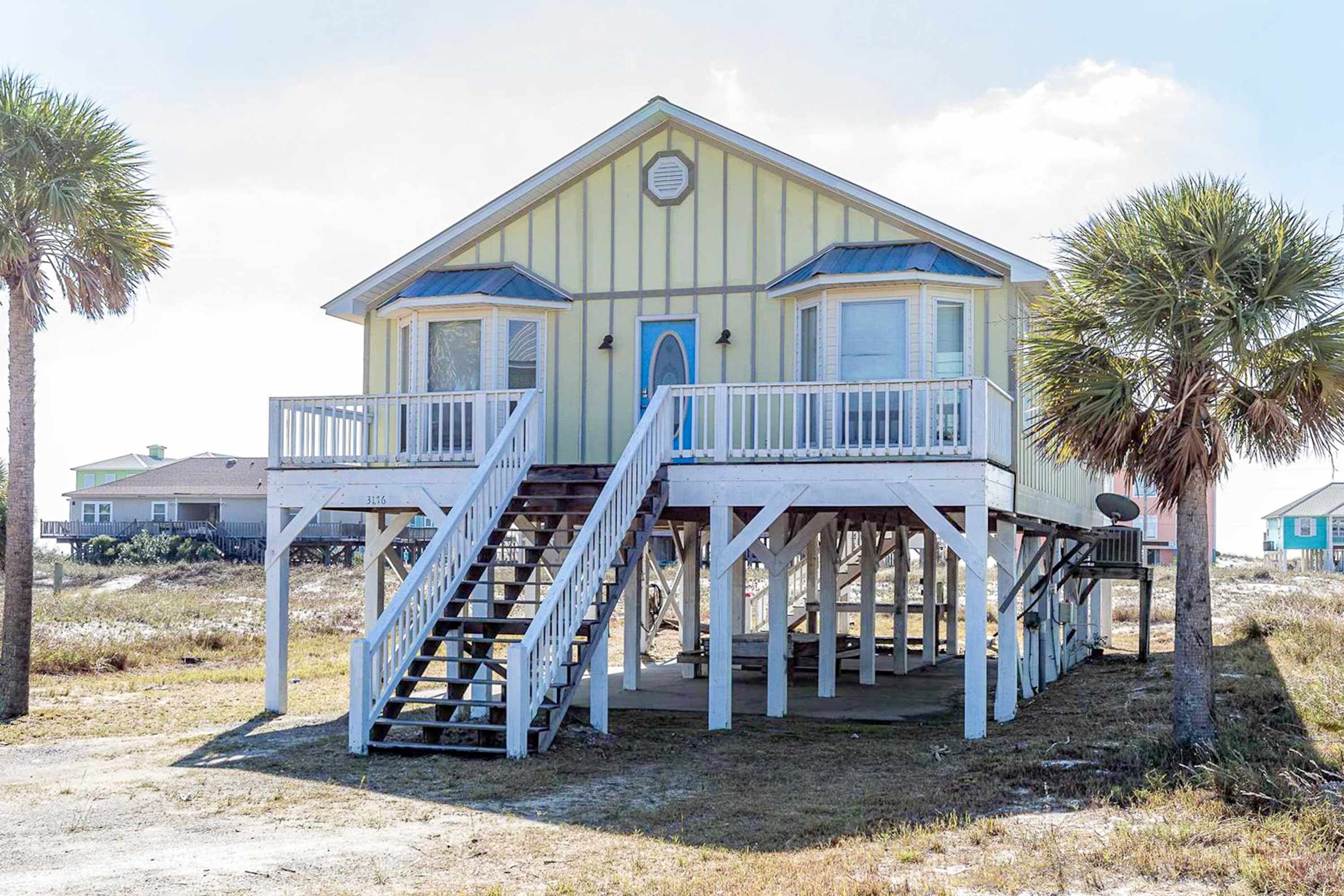 Una casa sulla spiaggia con un balcone, delle scale e un'entrata.
