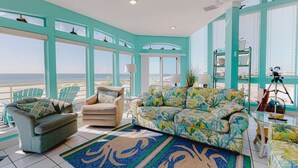 Una stanza con vista sulla spiaggia, una parete color acquamarina, un divano, due poltrone e una ventola a soffitto.