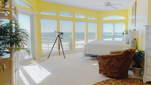 Una camera da letto con un letto, una poltrona marrone, un telescopio e vista sull'oceano attraverso ampie finestre.