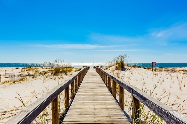 A wooden boardwalk leading to a beach with sand dunes and a clear blue sky. - Plantation Palms #6205 with Resort Pools, Hot Tubs & Tennis, Steps to Beach (Fort Morgan)