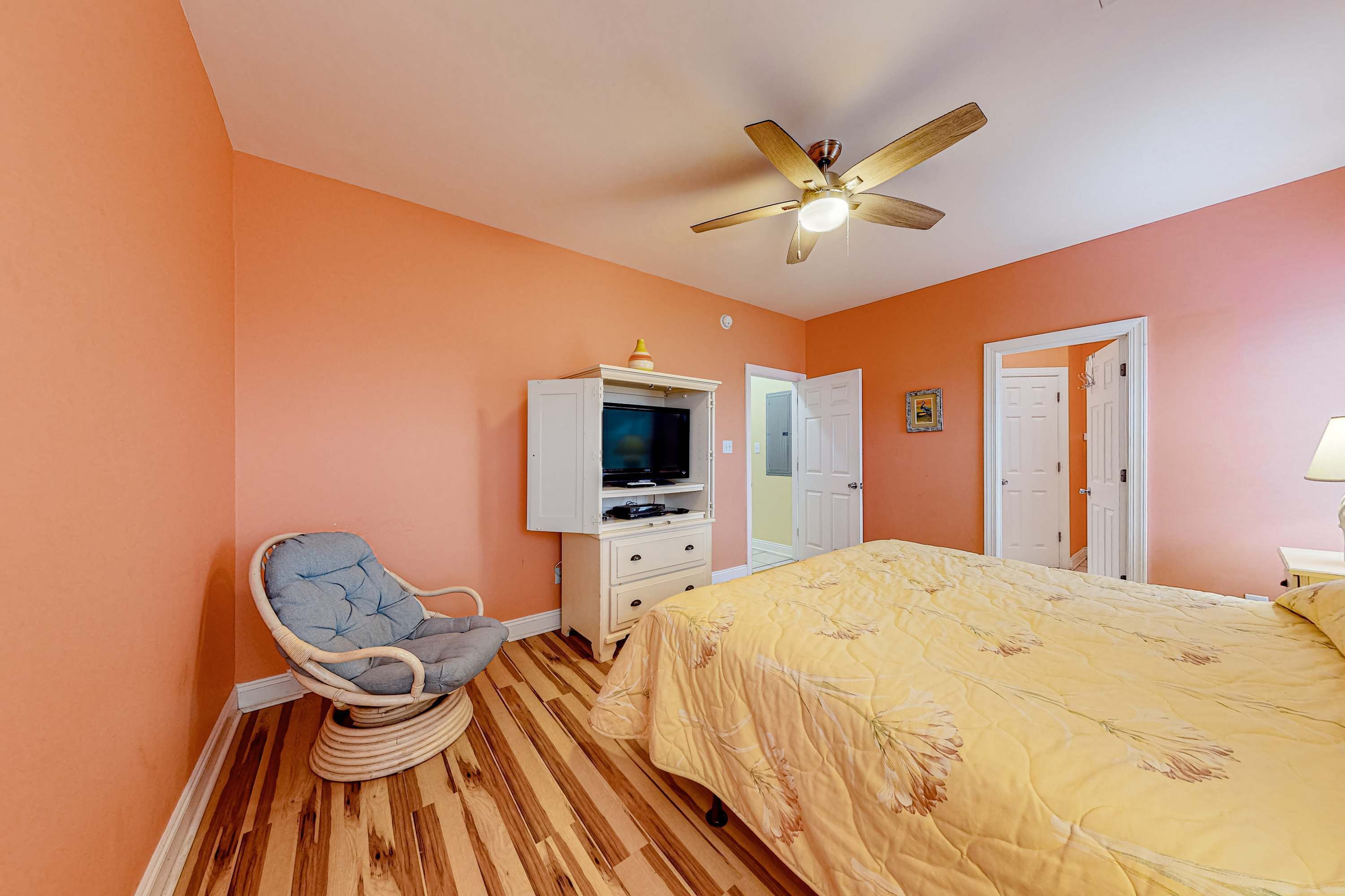 Une chambre à coucher avec un lit, une télévision, un ventilateur de plafond et une chaise.