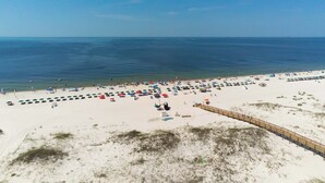 A beach with a wooden boardwalk, sandy beach, and umbrellas. - Snowbird-friendly condo with WiFi, on-site pools, hot tub, golf, & tennis (Gulf Shores)