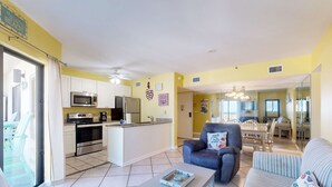 A modern kitchen with a central island, a dining area with a chandelier, and a living room with a sofa and armchair. - Snowbird-friendly condo with WiFi, on-site pools, hot tub, golf, & tennis (Gulf Shores)