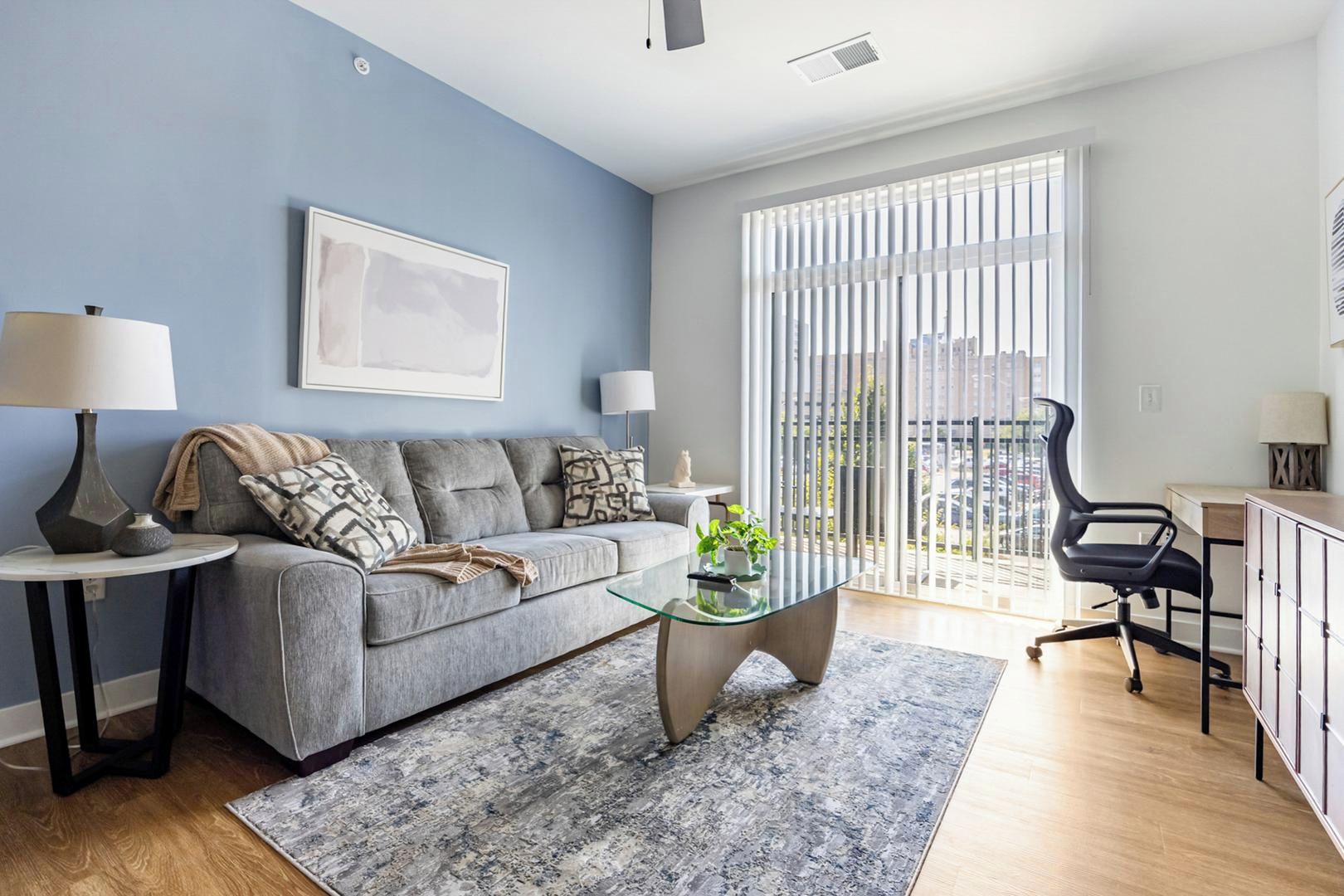 En moderne stue med en grå sofa, et glasbord og en sort kontorstol.