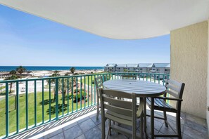 Een balkon met een tafel en stoelen, met uitzicht op een strand en een resortgebouw.