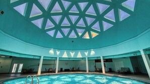 An indoor swimming pool with a geometric ceiling design, clear pool water, and multiple seating areas. - Spacious condo with balcony and shared pools and tennis, on-site golfing (Gulf Shores)