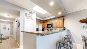 A modern kitchen with a central island, bar stools, and a microwave. - Updated 5th-floor condo with Gulf view, balcony, pool, & hot tub - near beach (Fort Morgan)