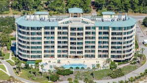 A multi-story hotel with a central courtyard, balconies, and a swimming pool. - Updated 5th-floor condo with Gulf view, balcony, pool, & hot tub - near beach (Fort Morgan)