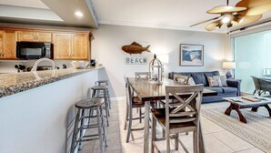 A modern kitchen with wooden cabinets, a microwave, and a dining area with a wooden table and chairs. - Updated 5th-floor condo with Gulf view, balcony, pool, & hot tub - near beach (Fort Morgan)