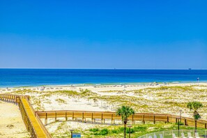 Una playa con un paseo marítimo de madera, dunas arenosas y un cielo azul despejado.