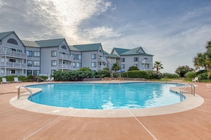 A swimming pool with a curved edge, surrounded by lounge chairs and a building with multiple balconies. - Second-floor condo with pool, hot tub, ocean view, fast WiFi & central AC (Fort Morgan)